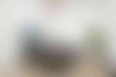 A spacious conference room with a long, polished wooden table surrounded by cushioned ergonomic chairs. Floor-to-ceiling windows allow natural light to flood the space, complemented by modern pendant lights and a large digital screen on the wall for presentations.