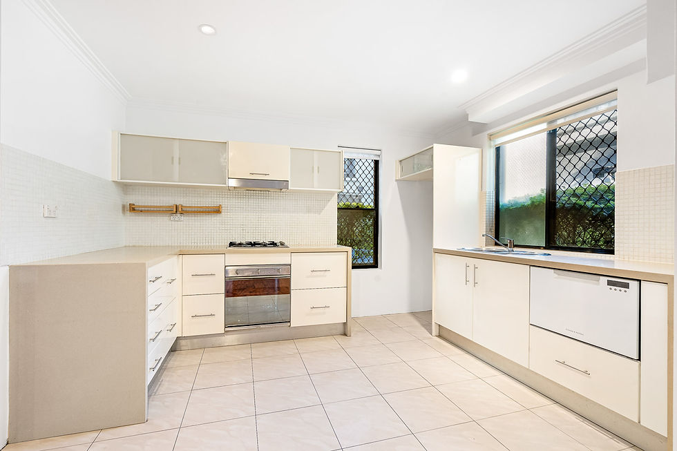 Modern kitchen with beige cabinets, gas stove, dishwasher, and tiled floor. Large windows with a garden view add brightness to the space.