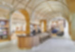 Modern store interior with curved arches, golden tones, plush seating, and displays of textiles. A sign reads "Joss & Main." Bright lighting.