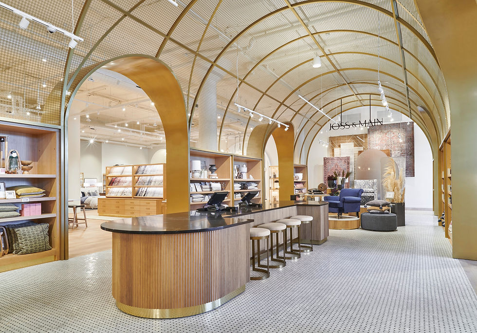 Modern store interior with curved arches, golden tones, plush seating, and displays of textiles. A sign reads "Joss & Main." Bright lighting.