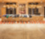 Jeans displayed on a log counter with stools in a store. Rustic decor with rope lights, wood shelves, art, and a zigzag red-orange rug.