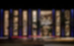 Night view of Bucherer 1888 store with illuminated windows, vertical blue lines, trees, and blurred car lights on the street.