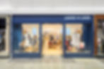 Storefront of Janie and Jack with mannequins in kids' clothing, bright interior and blue exterior. Signage reads "JANIE AND JACK."
