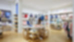 Janie and Jack store with neatly arranged colorful clothes on racks and shelves, wood floor, and bright lighting. Calm and organized setting.
