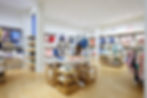 Janie and Jack store with neatly arranged colorful clothes on racks and shelves, wood floor, and bright lighting. Calm and organized setting.