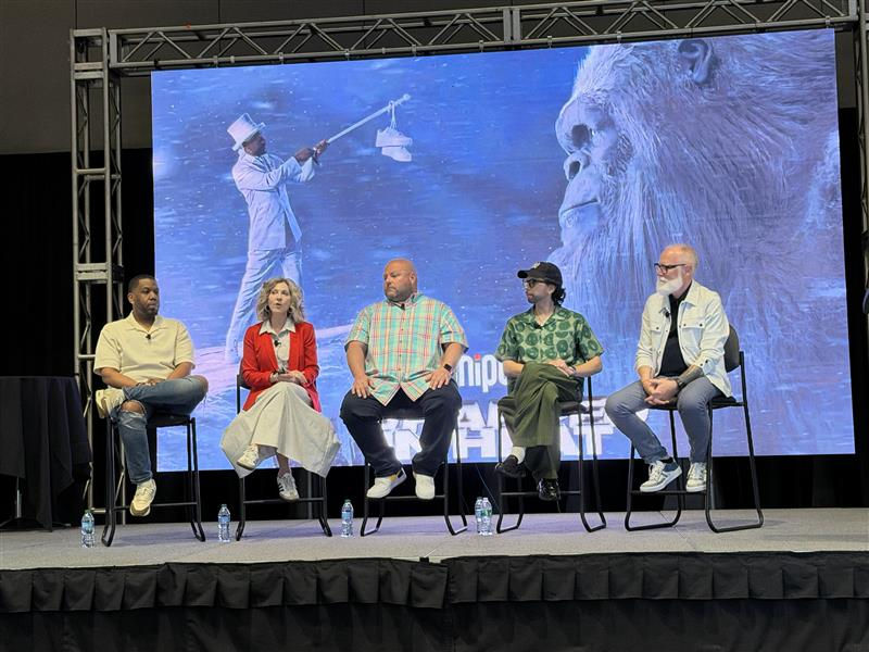 Five people seated on stage in front of a screen showing a gorilla and man in white suit. Casual attire, panel discussion setting.
