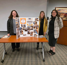 Three women presenting a poster for a leadership program.