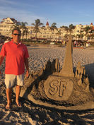 Man posing next to intricate sand sculpture of San Francisco