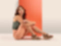 Woman in stylish sandals sitting against coral backdrop
