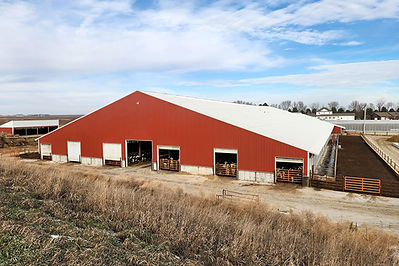 Red barn with open doors and agriculture setting under a blue sky.