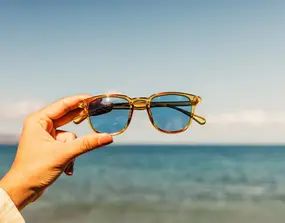 Hand holding stylish sunglasses, ocean view
