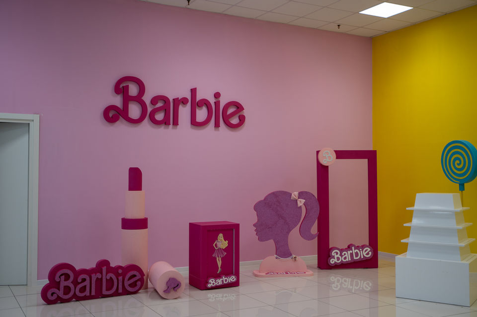 Esposizione "Barbie" con logo, rossetto, sagoma e scatola gigante su sfondo rosa.