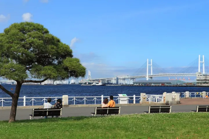 橫濱山下公園海濱步道，遊客坐在長椅上眺望橫濱海灣大橋與湛藍海景