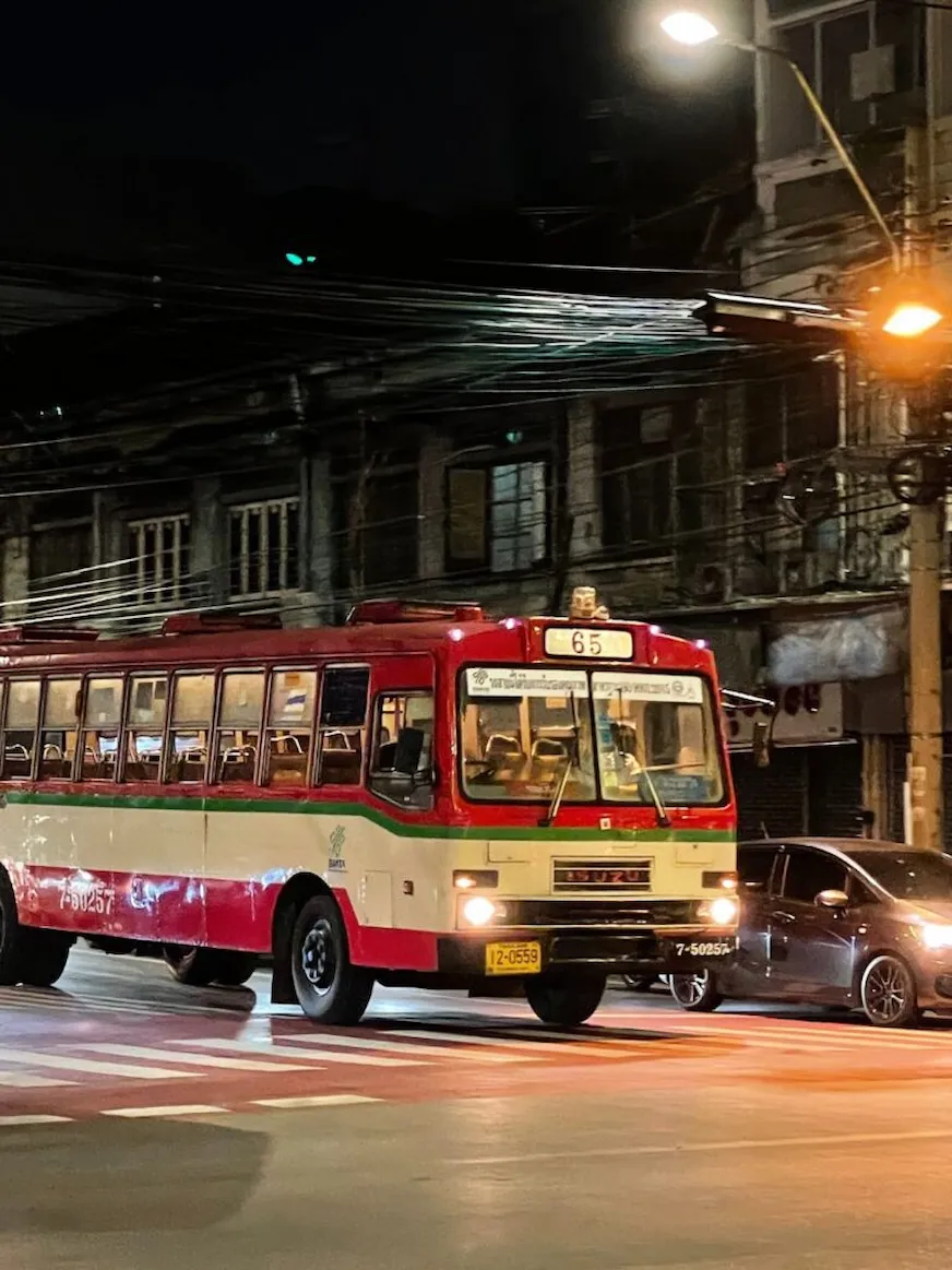 一輛於夜晚行駛於曼谷街頭的紅白相間公車