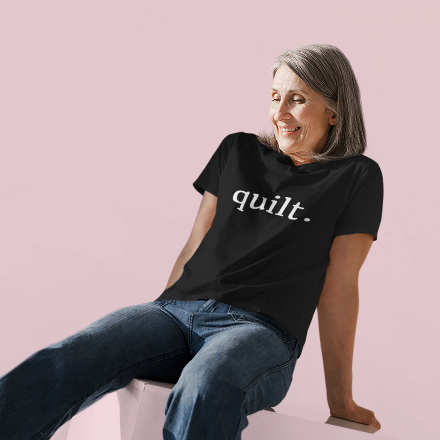 Katie's Quilting Co.'s black graphic tee with "quilt." in white modeled by a sitting woman with grey hair