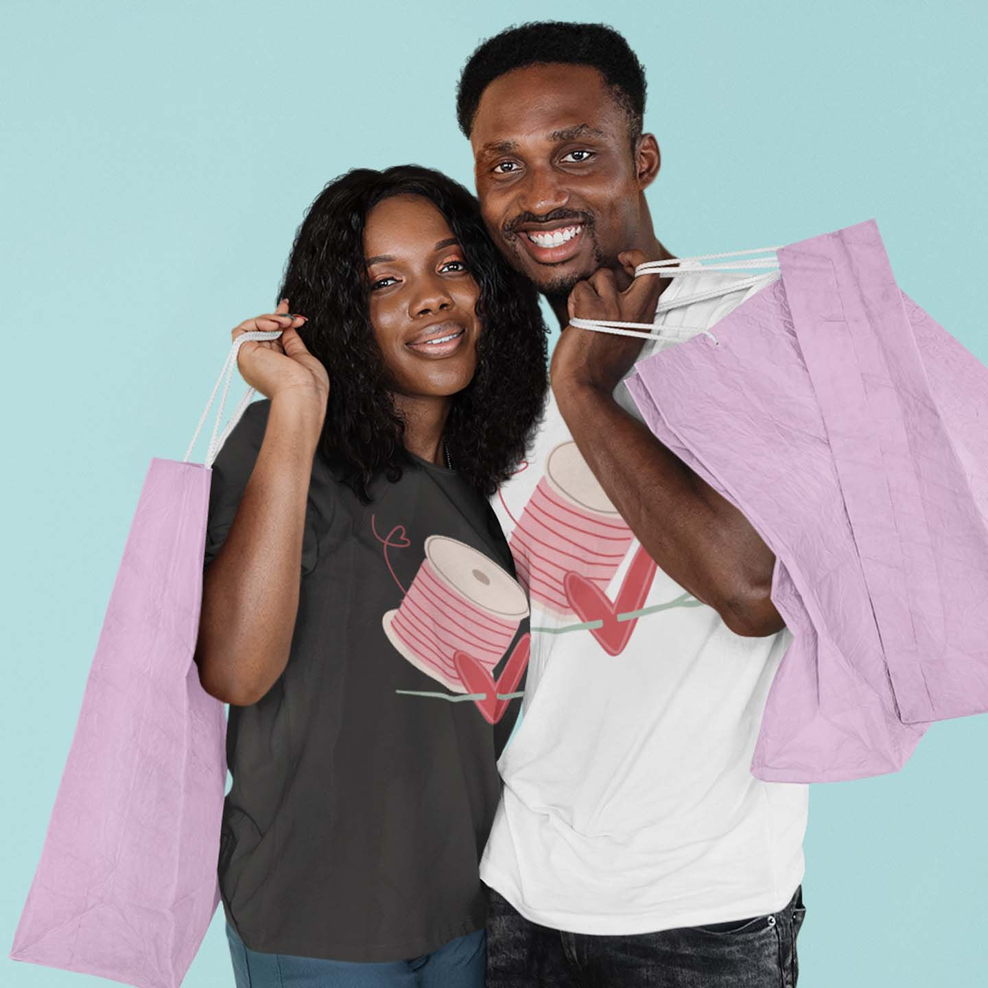 Graphic tee with hand-drawn pink spool of thread behind a heart being pierced by a needle modeled by a woman and man