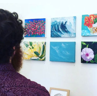 A person viewing several small painting exhibits on a wall.