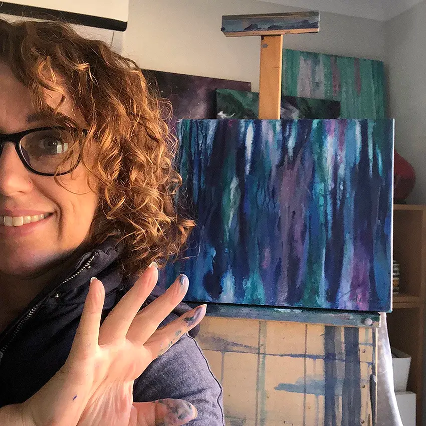 Smiling artist holding abstract blue and purple painting