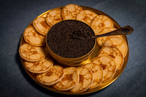 A shot of a golden plate with a large pot of black caviar surrounded by Bellini's.