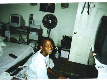 A black kid sitting down playing the video game.