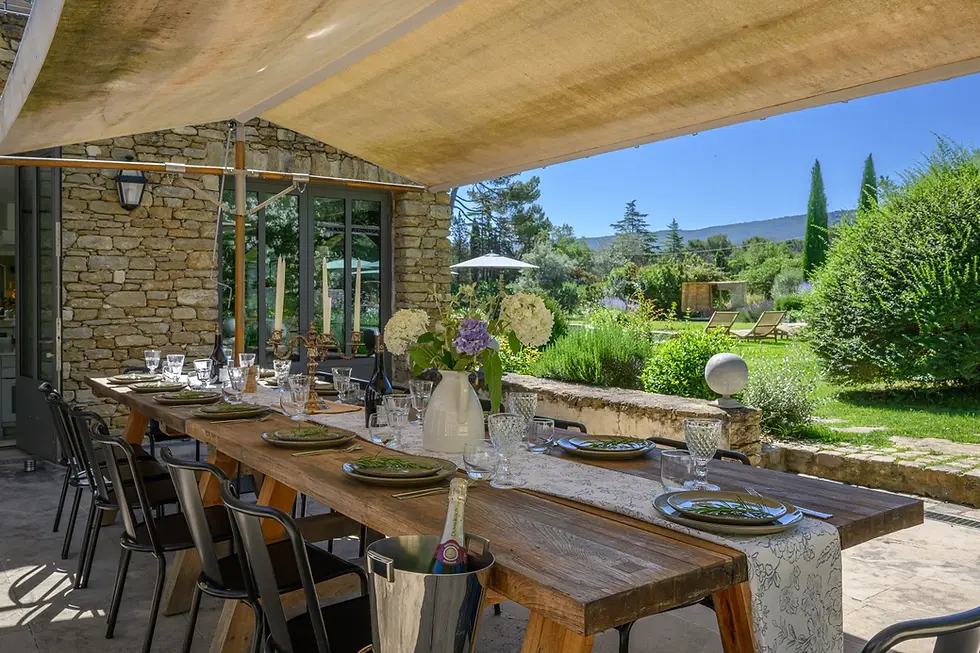 Longue table de repas sous le préau, ouverte sur le jardin de la Maison Yomana
