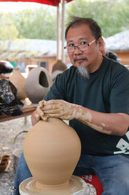 Cheah Yeow Seng making a pottery vase on a wheel while looking at camera.