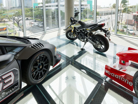 Two cars and a motorcycle on display on a glass floor.