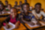 A classroom of children, with 3 looking up from their workbooks