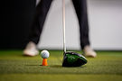 Golf ball teed up on turf at an indoor golf simulator.