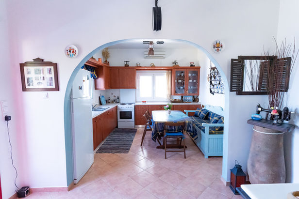 View from Ikarian Endless Blue master bedroom through open door: elegant entrance hall flowing into modern kitchen with Aegean Sea light, Ikaria Greece – luxury Blue Zone villa interior