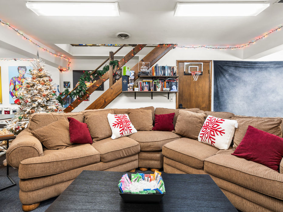 Front view of the main seating area in the Locked In podcast studio with sectional couch, holiday decor, bookshelf, and basketball hoop behind the set.