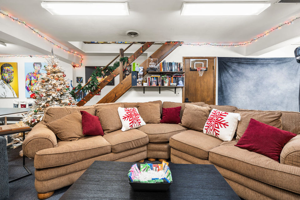 Front view of the main seating area in the Locked In podcast studio with sectional couch, holiday decor, bookshelf, and basketball hoop behind the set.
