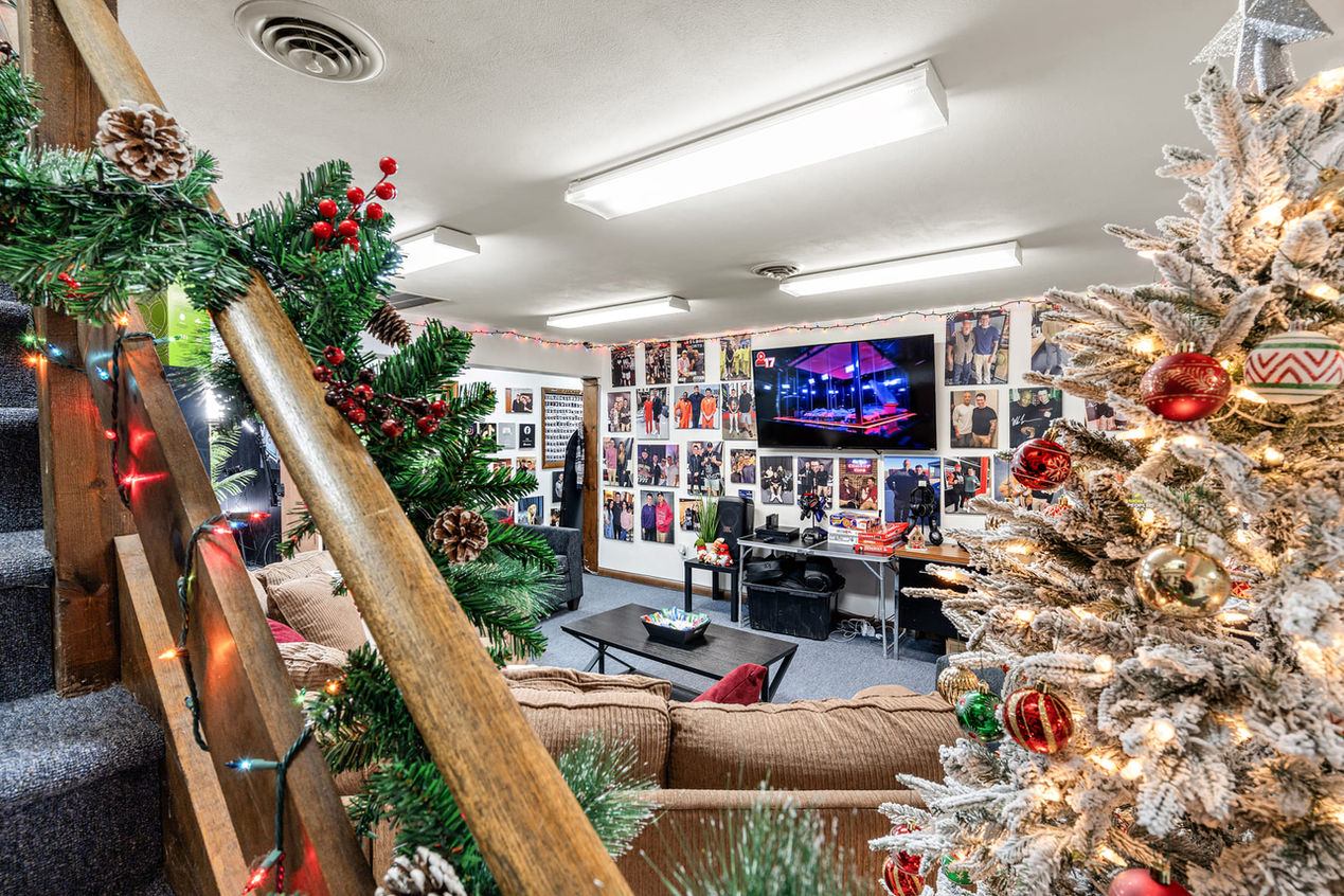 View from the staircase overlooking the main lounge with holiday decorations, seating area, and wall of guest photos in the Locked In studio.