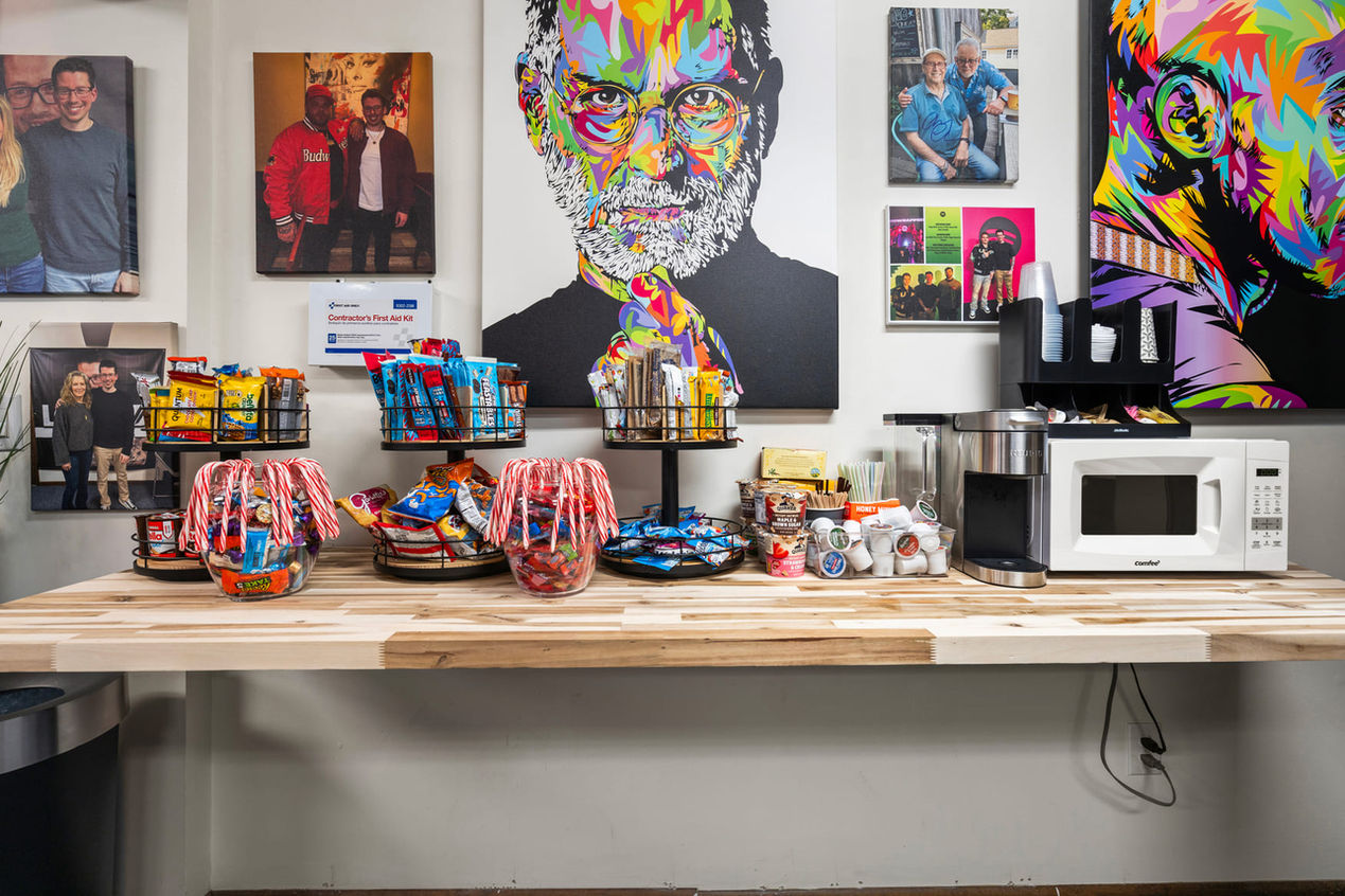 Community snack and coffee station inside the Locked In With Ian Bick studio featuring candy baskets, K-cups, microwave, and framed artwork.