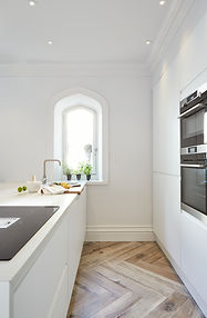 Contemporary white kitchen with an arched window, integrated ovens and herringbone flooring at Carter Manor, Wilmslow