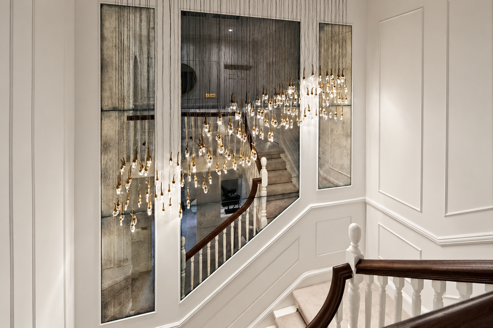 Staircase landing with antique mirror panelling and cascading bronze chandelier.