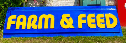 Antique commercial sign that reads "Farm and Feed" in big yellow letters with a blue background 