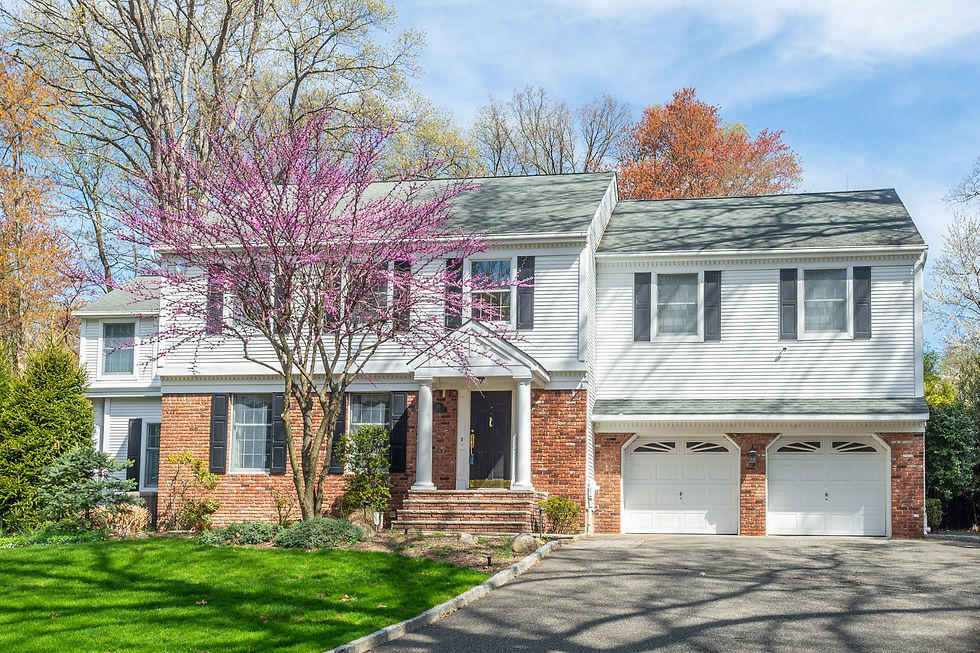 Stunning colonial-style home for sale in Allendale, NJ by The Gill Group, featuring white siding, red brick exterior, double garage, and landscaped cul-de-sac lot with blooming trees—Bergen County real estate at its finest.