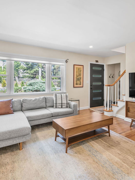 Bright living room in Harrington Park rental home with hardwood floors, gray sectional sofa, and large TV—perfect for relaxing in this modern Bergen County property.