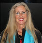 The poet Pam Uschuk with long ash-blond hair and light skin wearing a black shirt with turquoise scarf.
