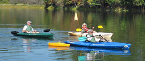 three people using adaptive kayaking gear paddling on a calm lake