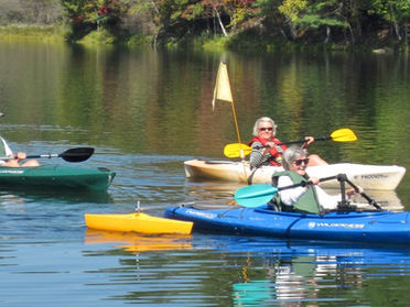 three people using adaptive kayaking gear paddling on a calm lake