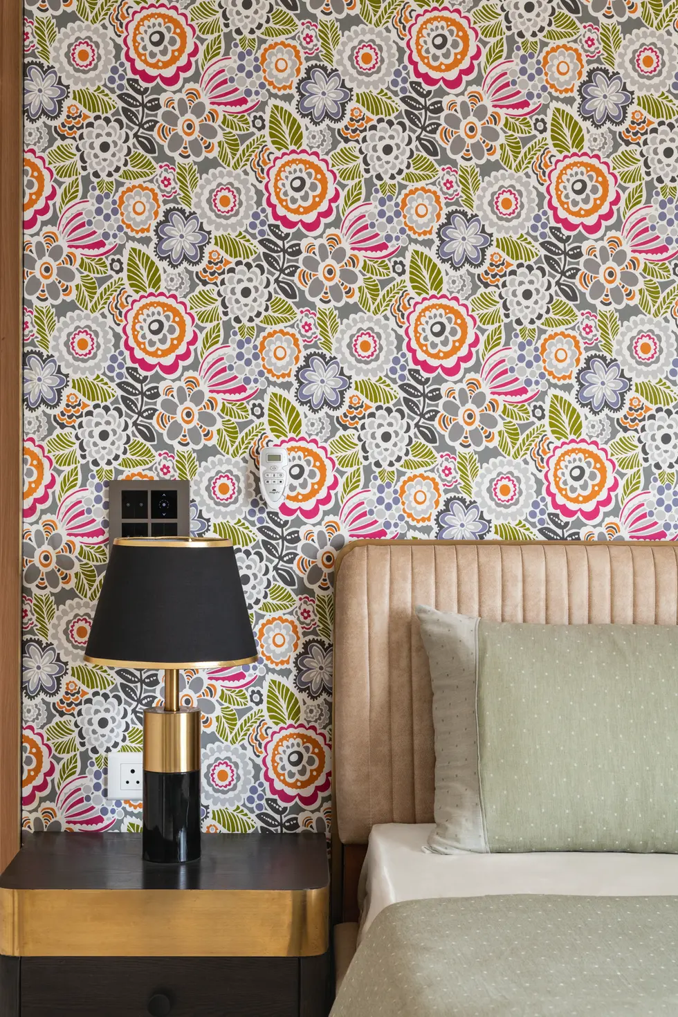 Vibrant bedroom interior featuring multicolored floral wallpaper, a beige fluted headboard, and a black and gold nightstand.