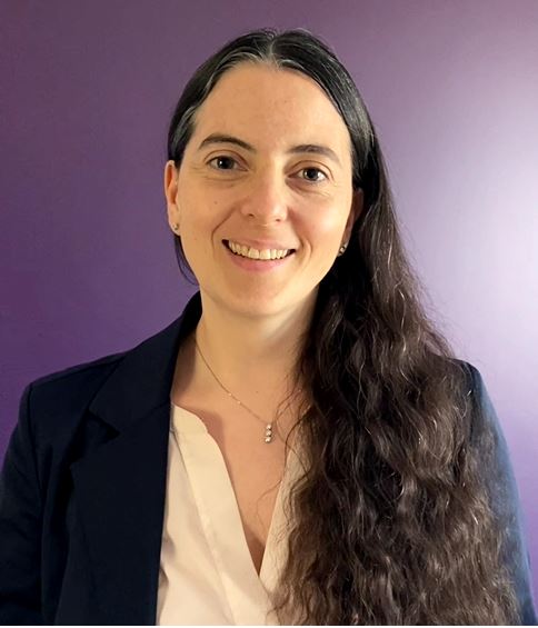 Femme souriante avec de longs cheveux bruns, veste sombre, fond violet, portrait.