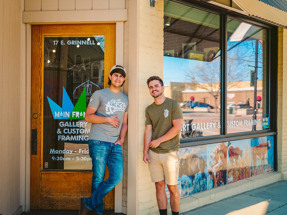 Micah and Nathan stand in front of their framing shop and smile for the camera