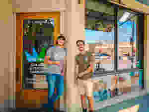 Micah and Nathan stand in front of their framing shop and smile for the camera