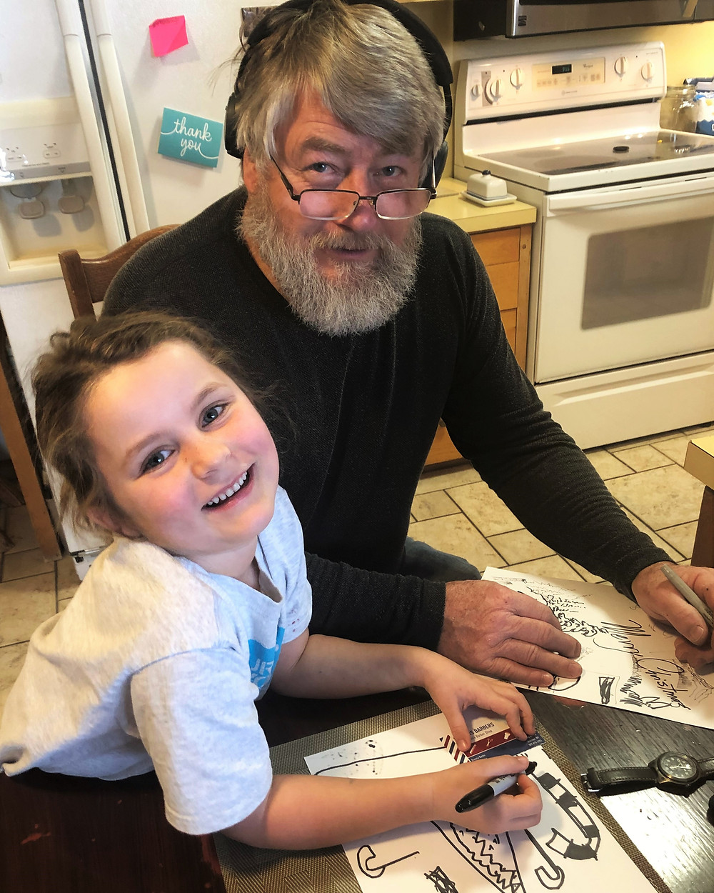 A little girl and her uncle smile at the camera while working on a drawing