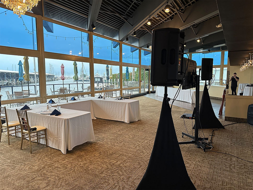 Indoor waterfront venue with professional speaker setup and banquet tables for a private event.