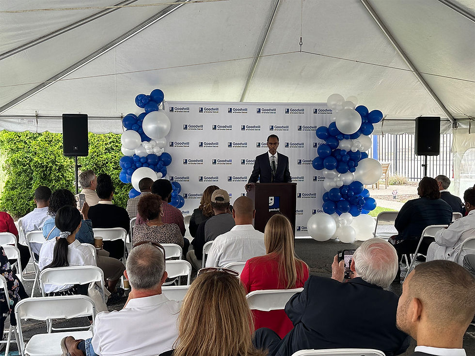Goodwill outdoor ceremony under event tent with speaker, sound system, and balloon backdrop.