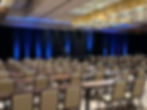 Blue uplighting on draped stage backdrop for corporate conference setup.